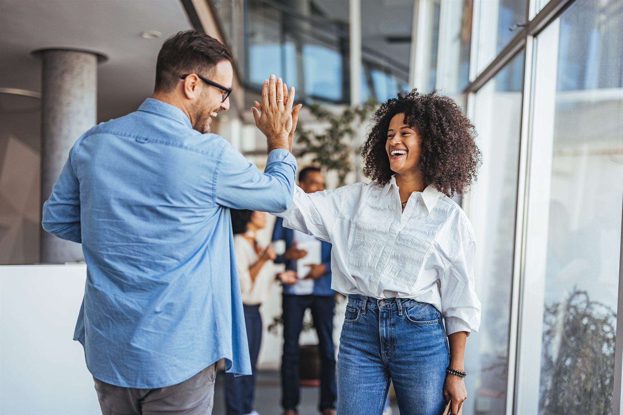 Zwei Kolleg:innen geben sich im Büro ein High-Five.